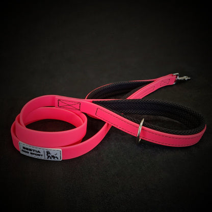 Pink and black dog leash with mesh handle and metal clasp on a dark surface.