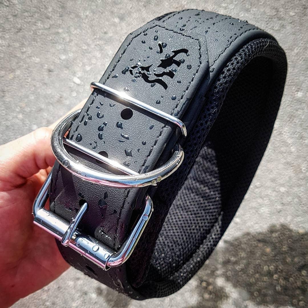 Black weightlifting belt with silver buckle and water droplets on textured surface.