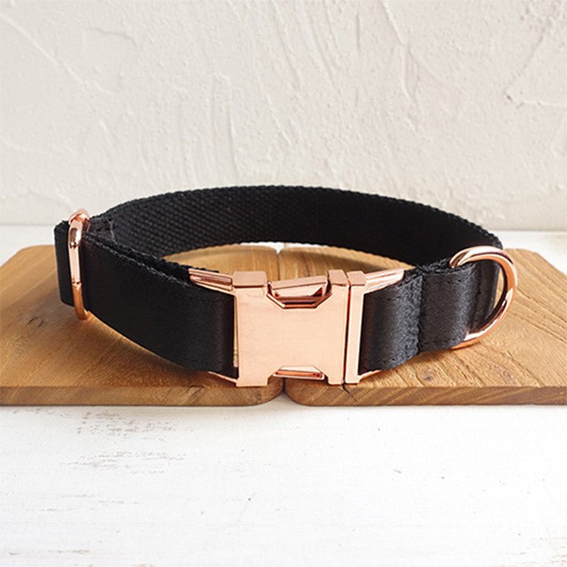 Black dog collar with rose gold buckle and hardware on a wooden surface.