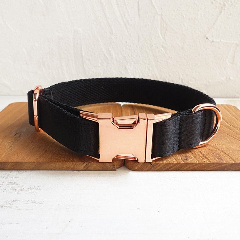 Black fabric dog collar with rose gold buckle and hardware, displayed on a wooden surface.