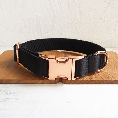 Black fabric dog collar with rose gold buckle and hardware, displayed on a wooden surface.