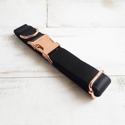 Black strap with rose gold buckles on a white wooden surface.
