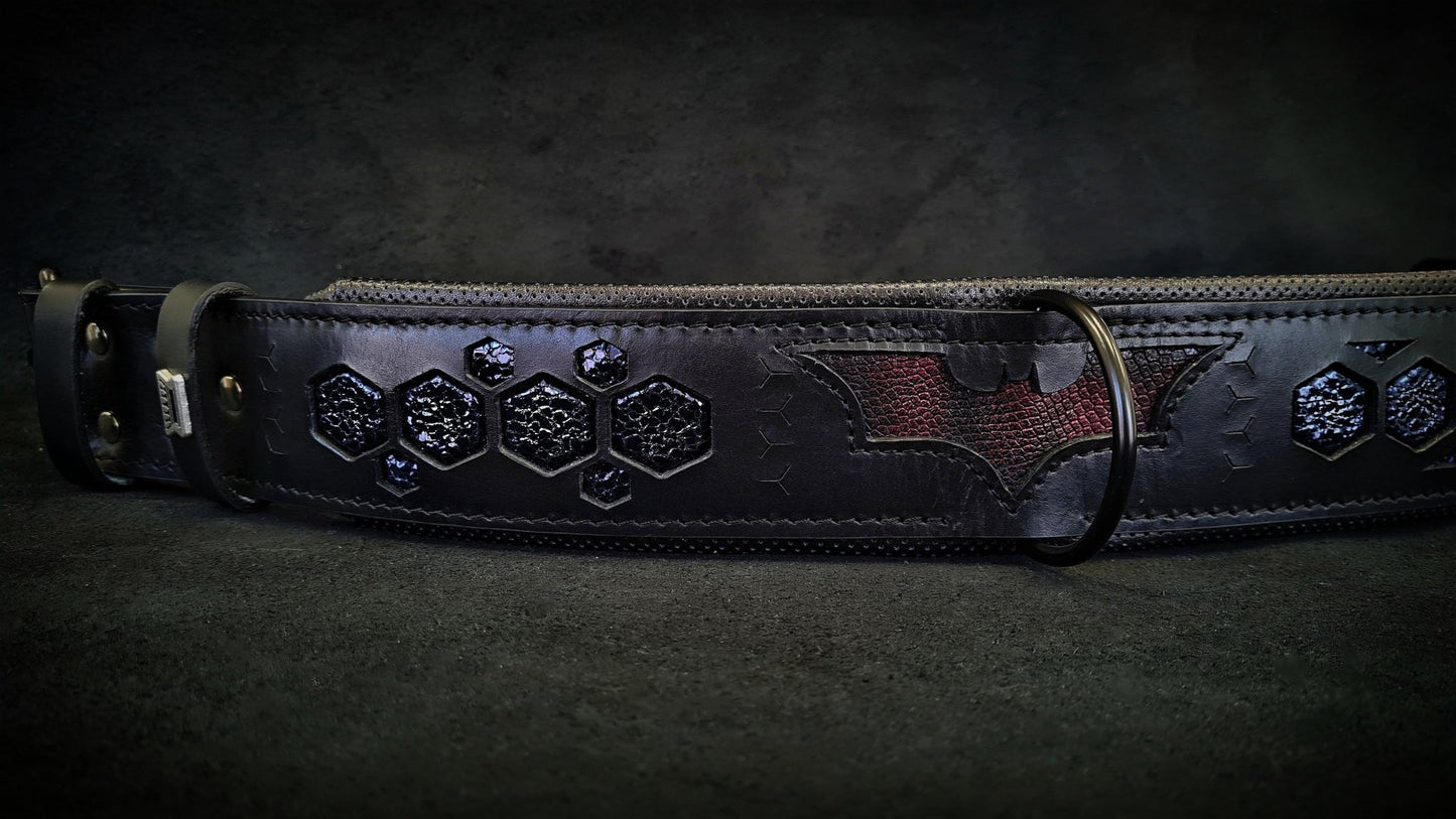 Black leather belt with embossed bat symbol and hexagonal patterns, displayed on a dark surface.
