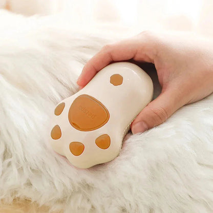Hand holding a white and orange paw-shaped pet grooming tool on a fluffy surface.