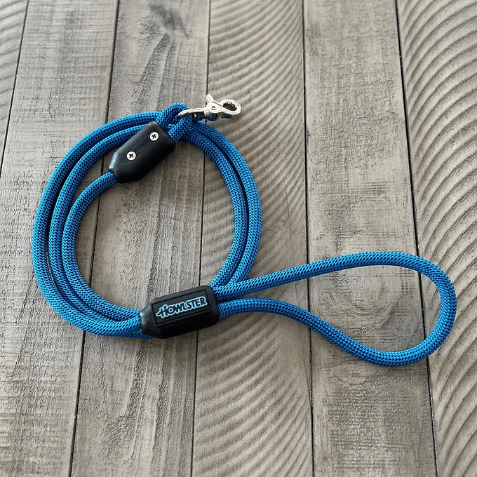 Blue braided dog leash with metal clasp and Howlster brand label on wooden surface.