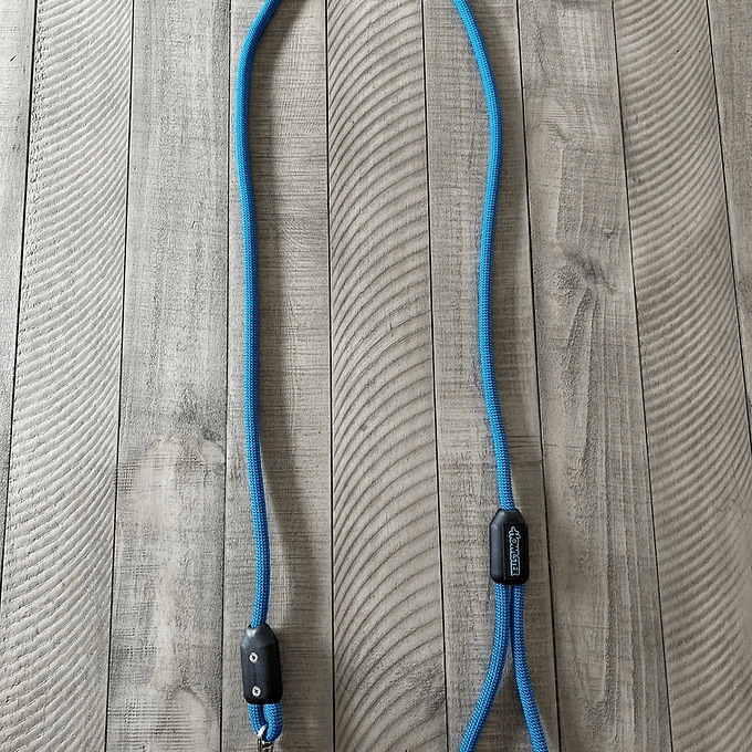 Blue braided rope leash with black plastic clips on a wooden surface.