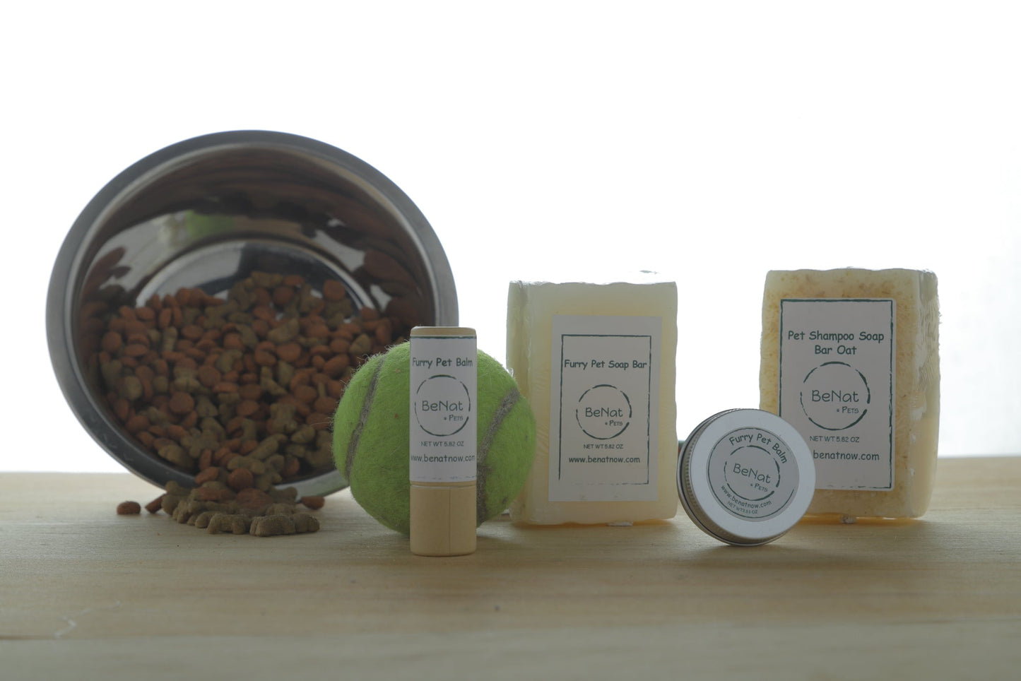 Pet grooming products including balm, soap bars, and a tennis ball on a wooden surface.