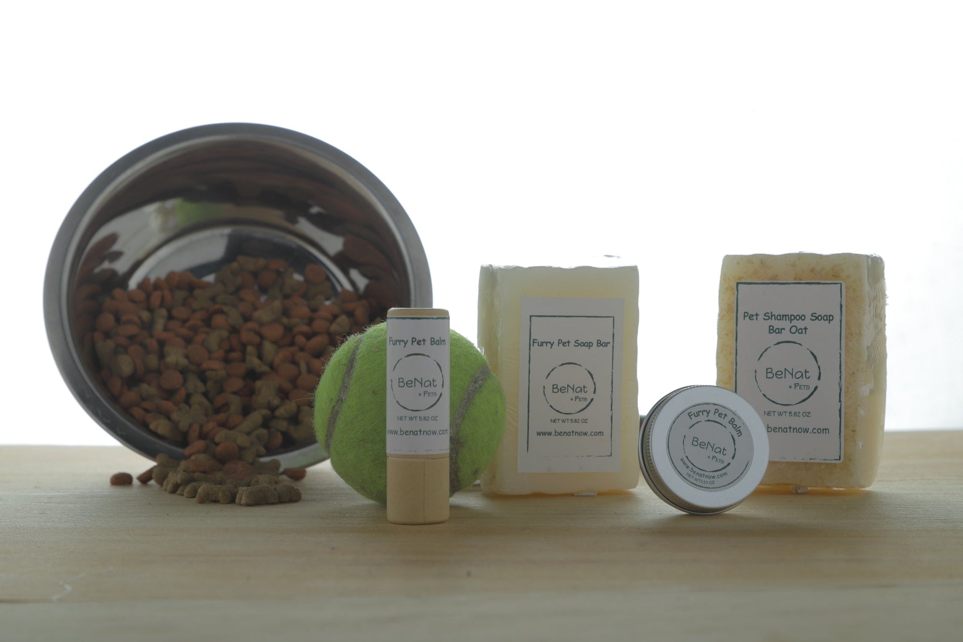 Pet grooming products including balm, soap bars, and a tennis ball on a wooden surface.