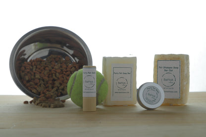 Pet grooming products including balm, soap bars, and a tennis ball on a wooden surface.